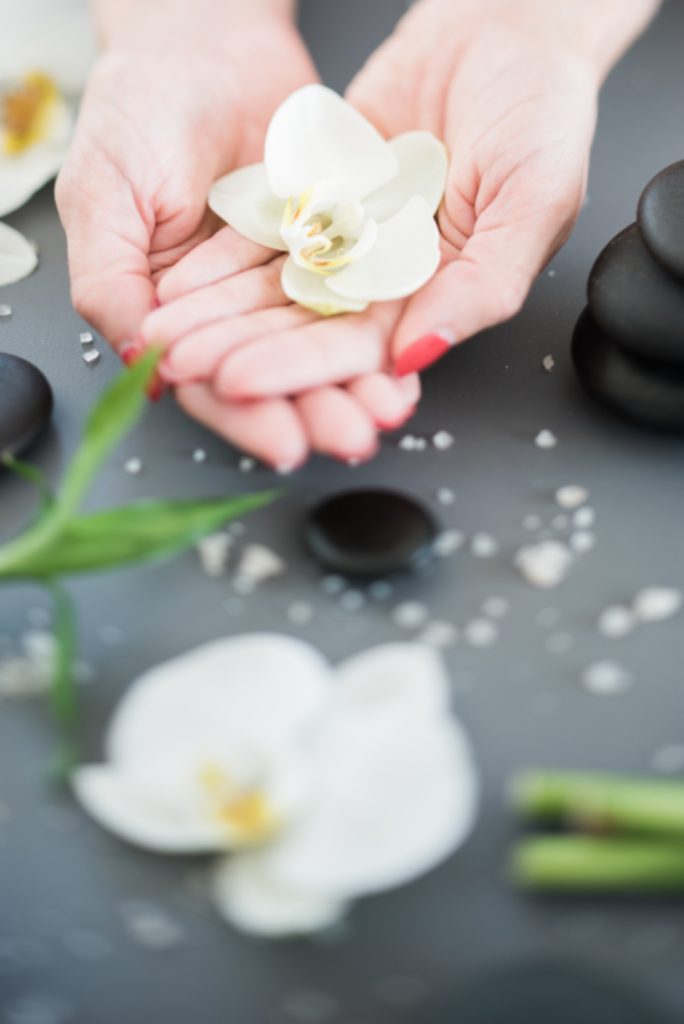 Handen houden een witte orchidee vast naast hotstones